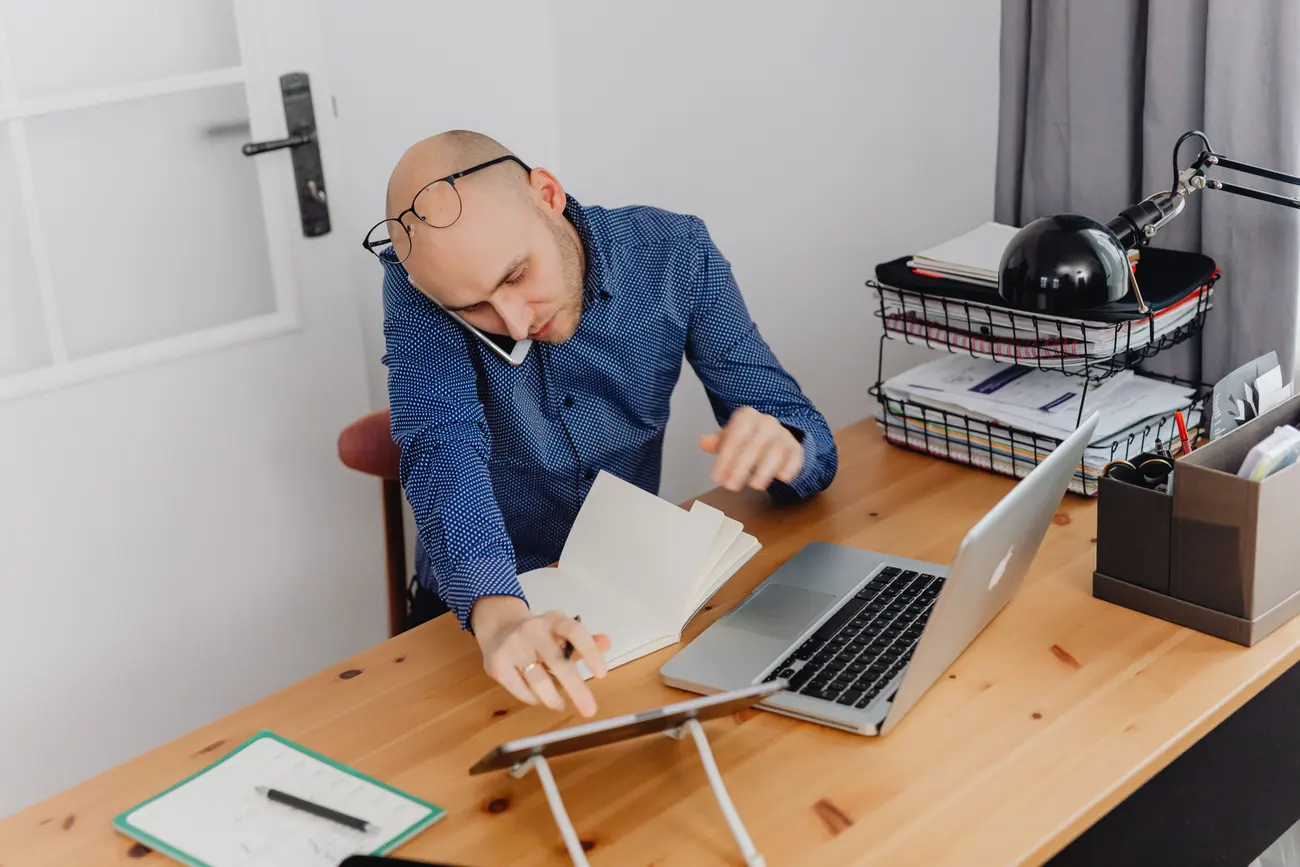 Mãos digitando no notebook em uma mesa de trabalho organizada, com bloco de notas ao lado