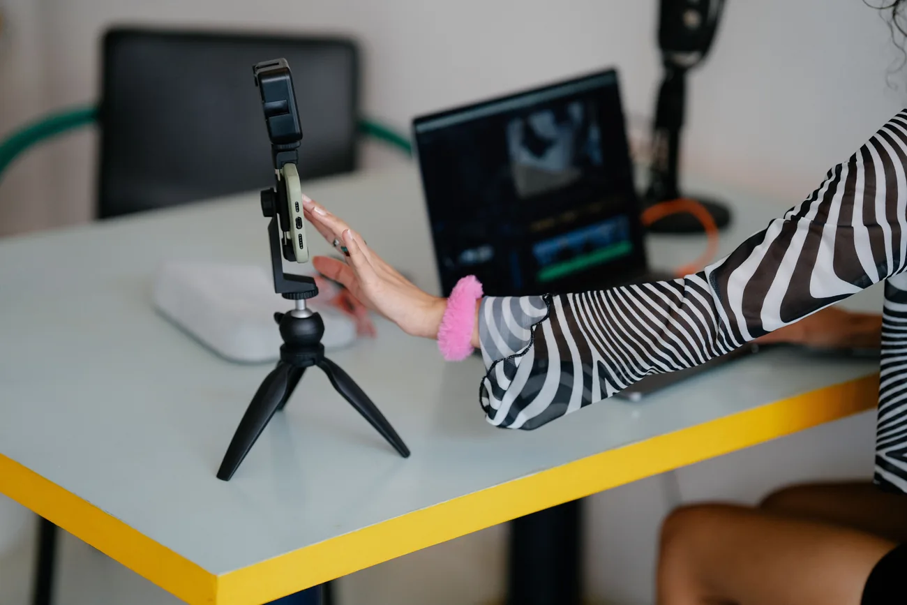 Celular num tripé de mesa ao lado de um notebook com programa de edição de vídeo aberto