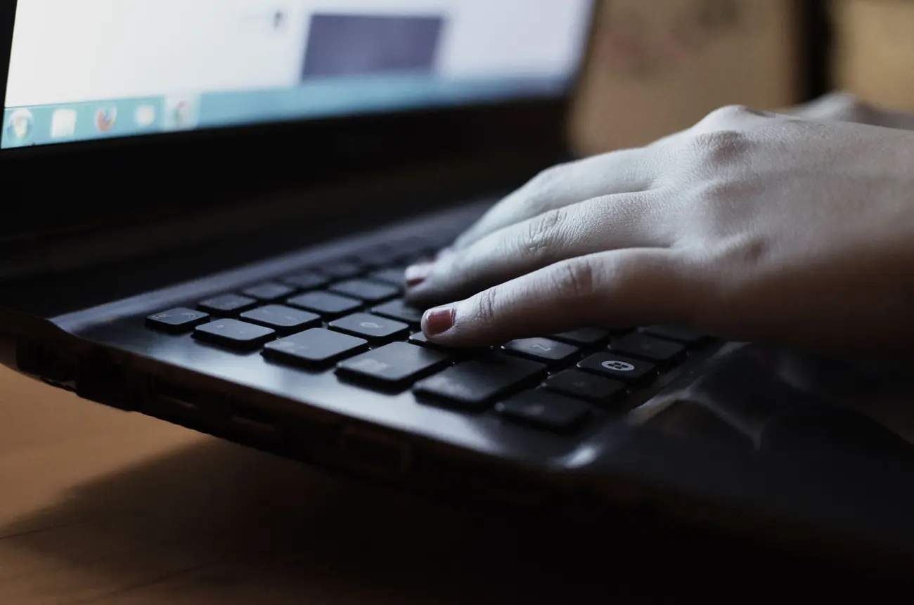 Close de mãos digitando no teclado do notebook em ambiente com pouca luz