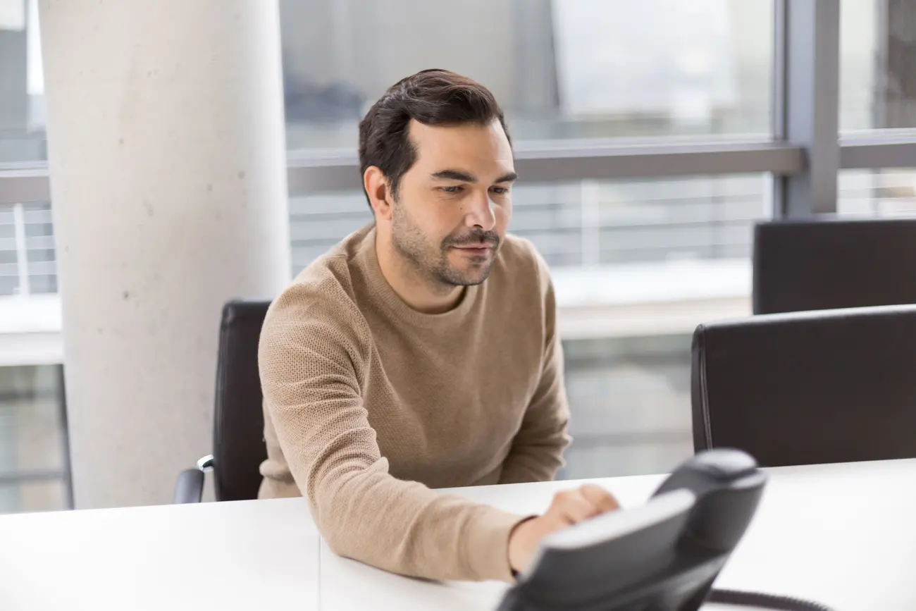 Homem olhando pensativo para o telefone da mesa, esperando uma resposta que não chega