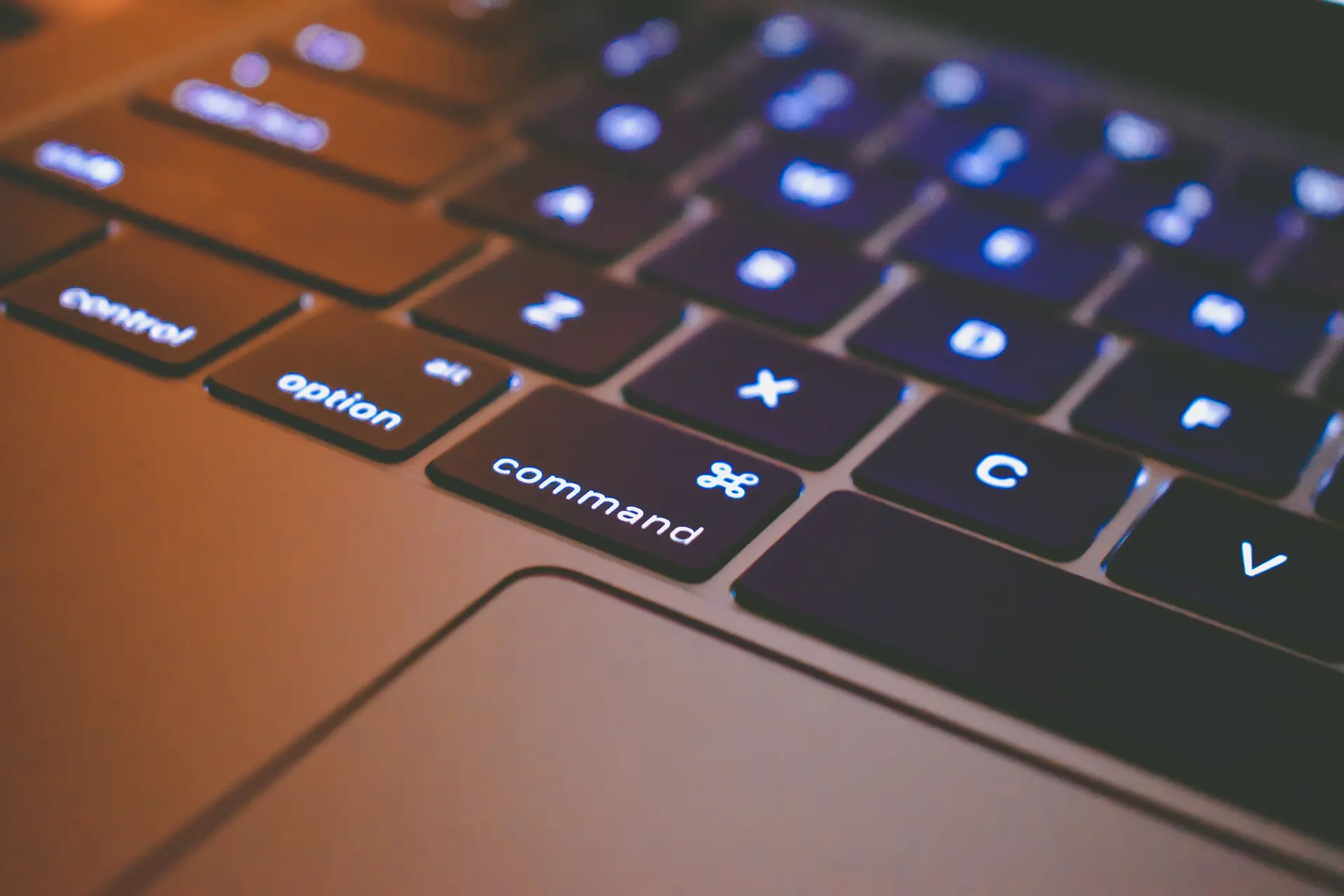 Teclado de notebook iluminado no escuro, com a tecla de comando em destaque