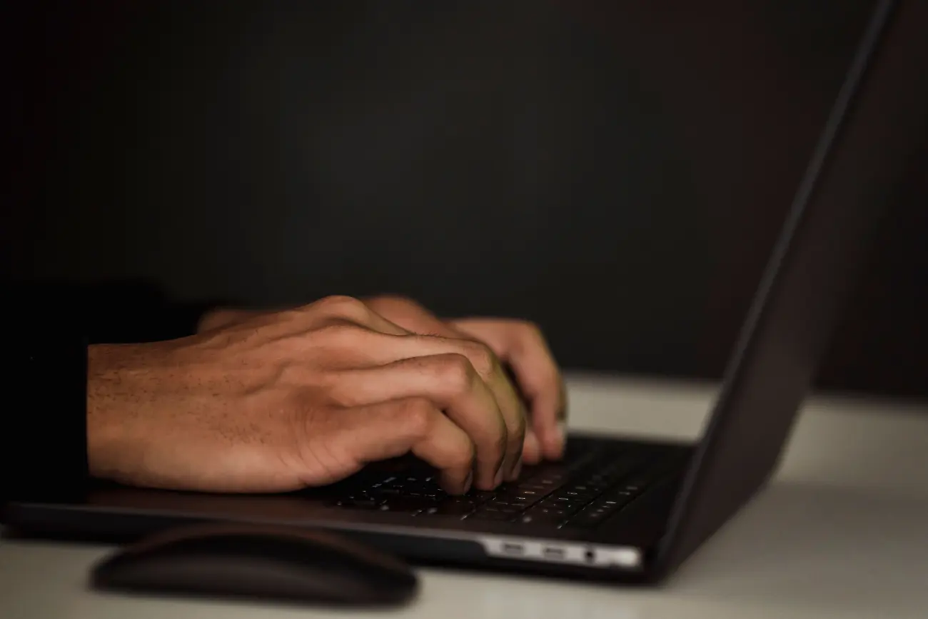 Mãos digitando no teclado de um notebook em ambiente escuro