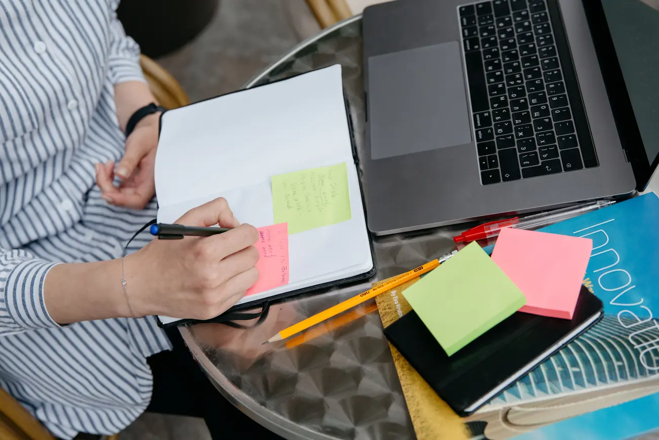 Mãos organizando post-its numerados ao lado do notebook, cada ideia separada em um bloco