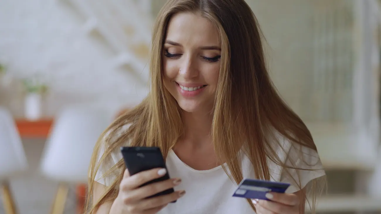 Cliente sorrindo enquanto usa o celular e o cartão para finalizar uma compra