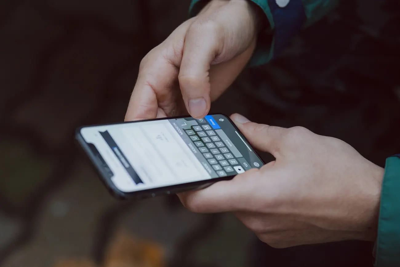 Mão digitando uma mensagem no celular em ambiente externo