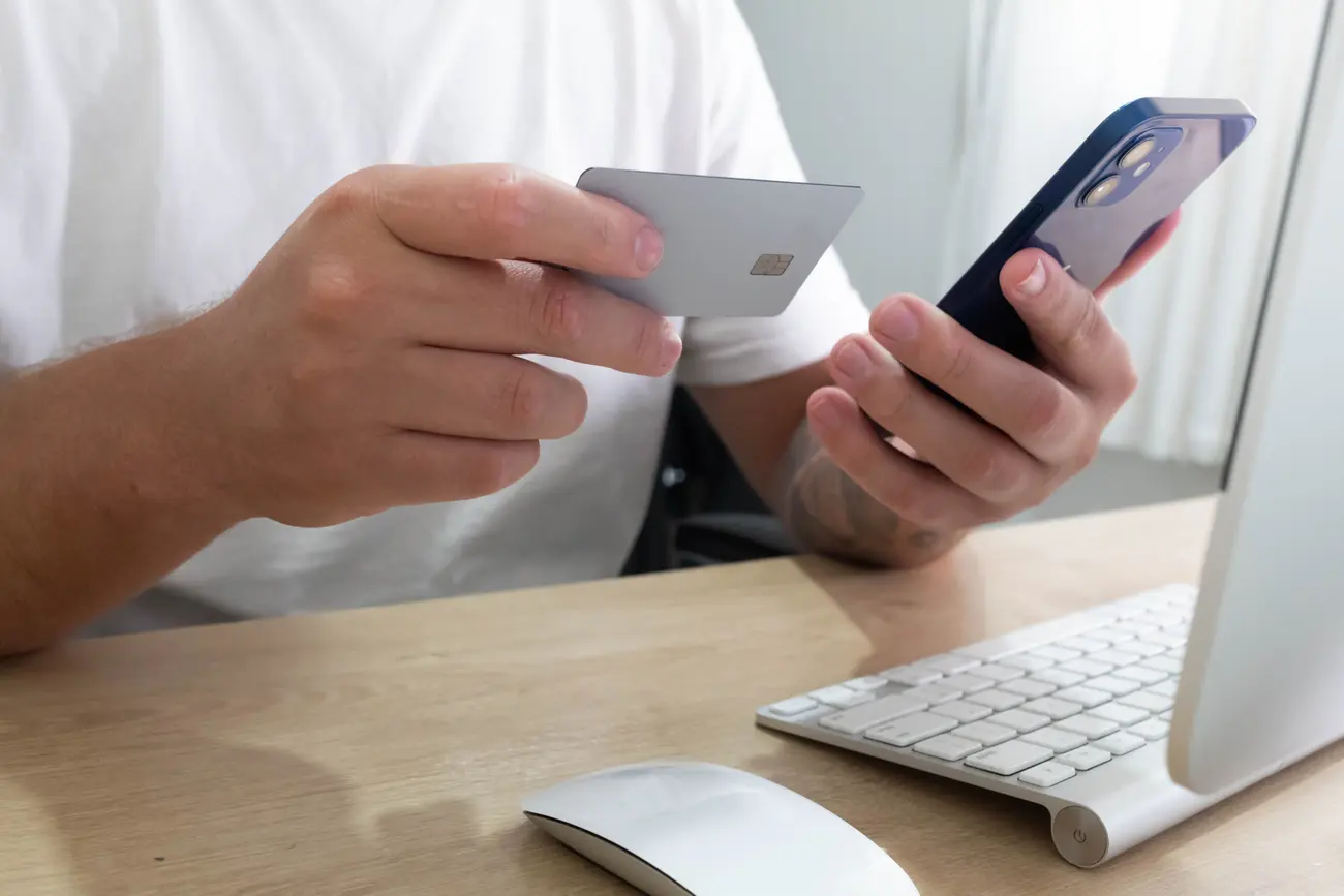 Mão segurando cartão e celular para finalizar uma compra online