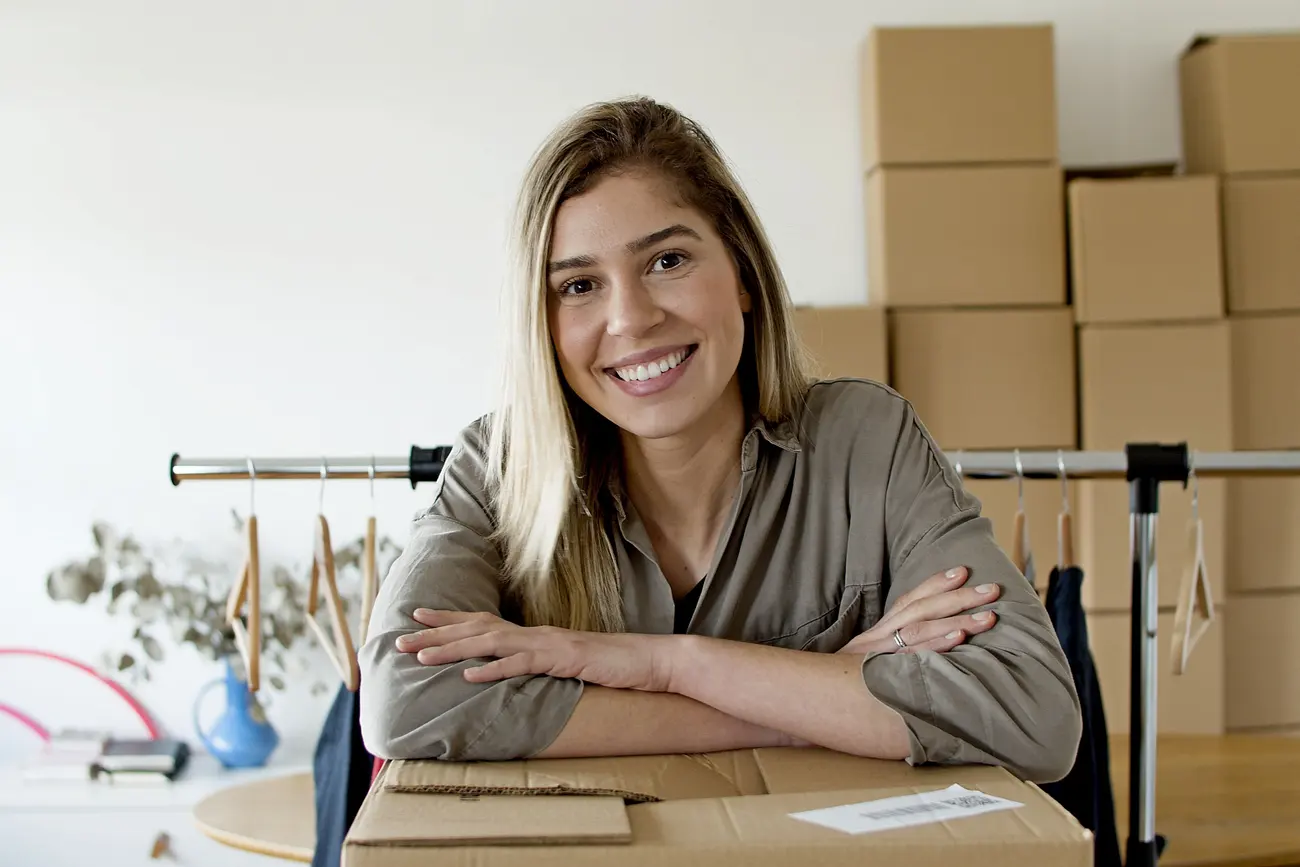 Dona de e-commerce de moda sorrindo ao lado do estoque de roupas