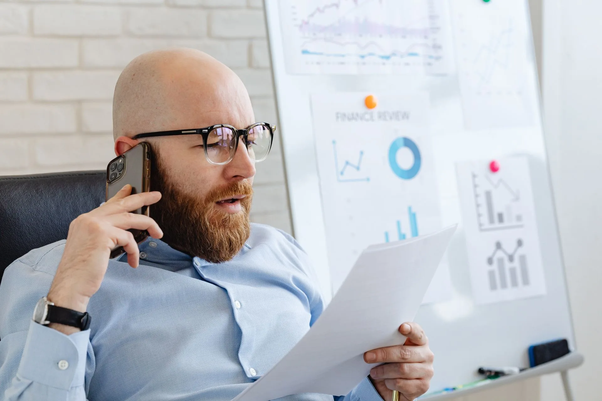 Empresário de óculos ao telefone conferindo um relatório impresso no escritório