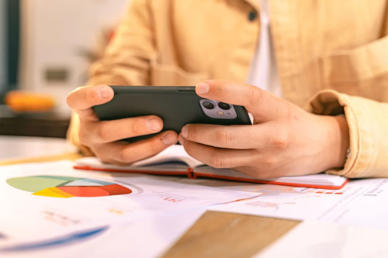 Pessoa segurando o celular na horizontal sobre uma mesa com gráficos impressos