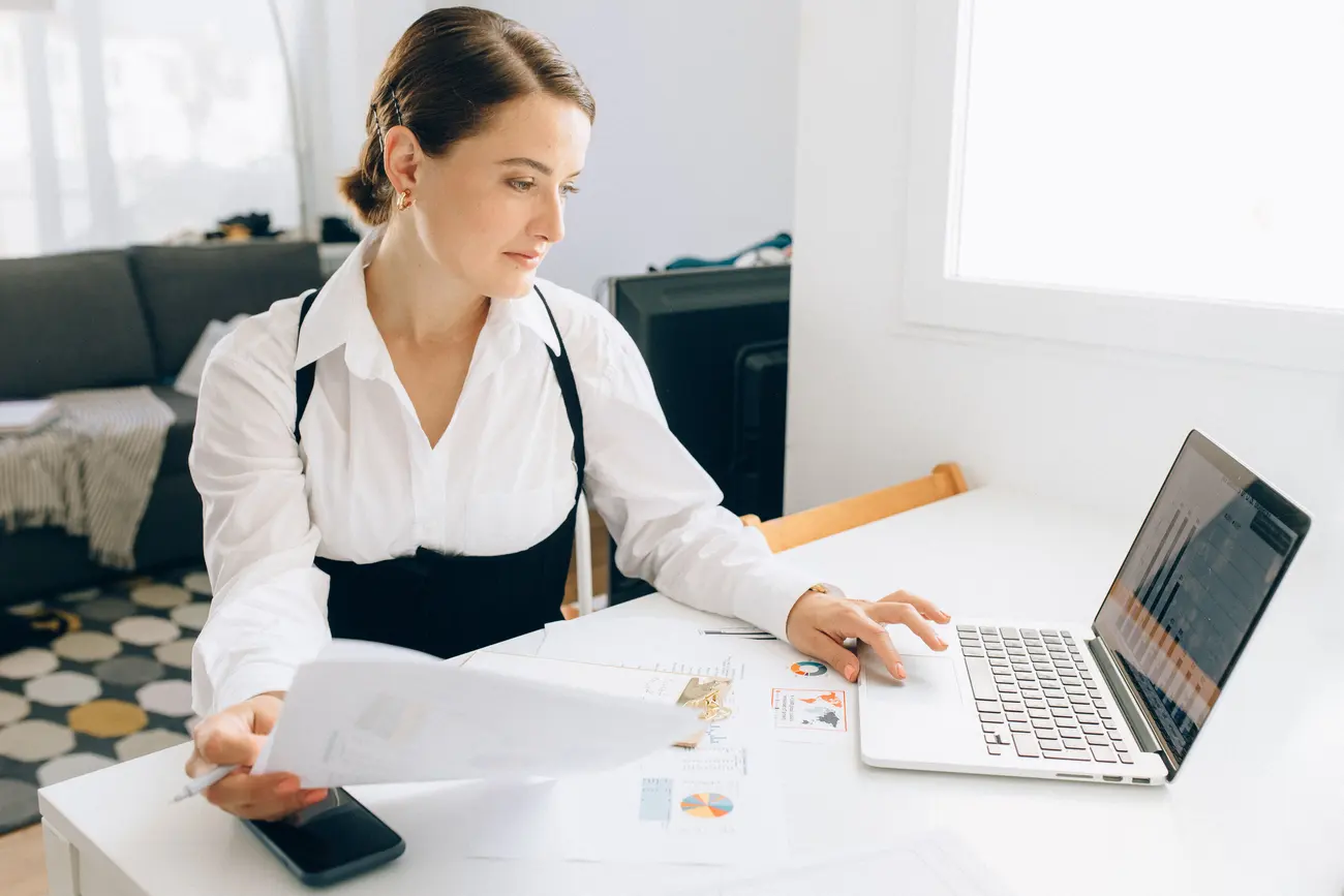 Mulher analisa papéis com gráficos de vendas ao lado do notebook