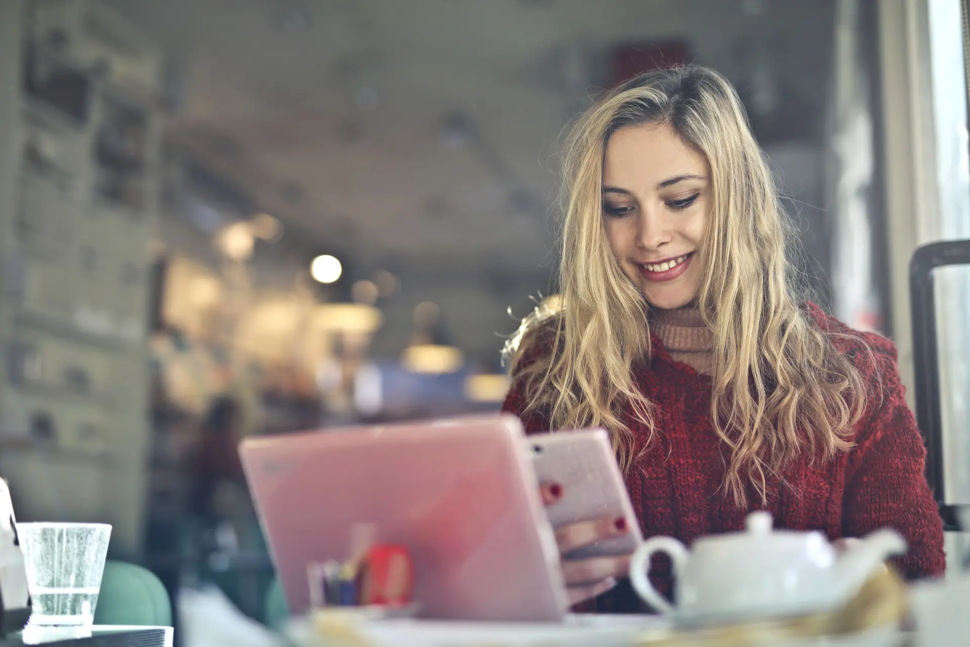 Mulher sorri olhando para o celular em um café, luz quente ao fundo