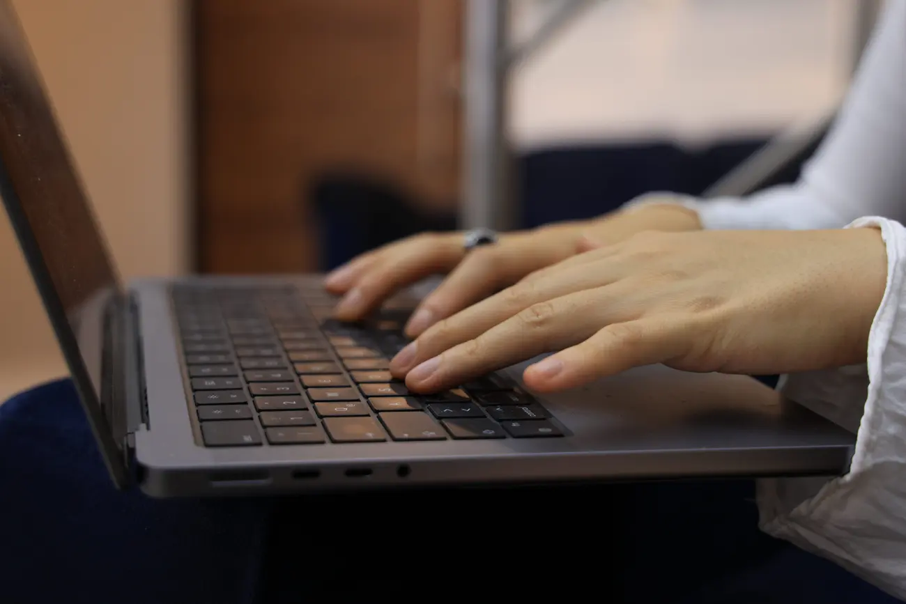 Mãos digitando no notebook em ambiente iluminado