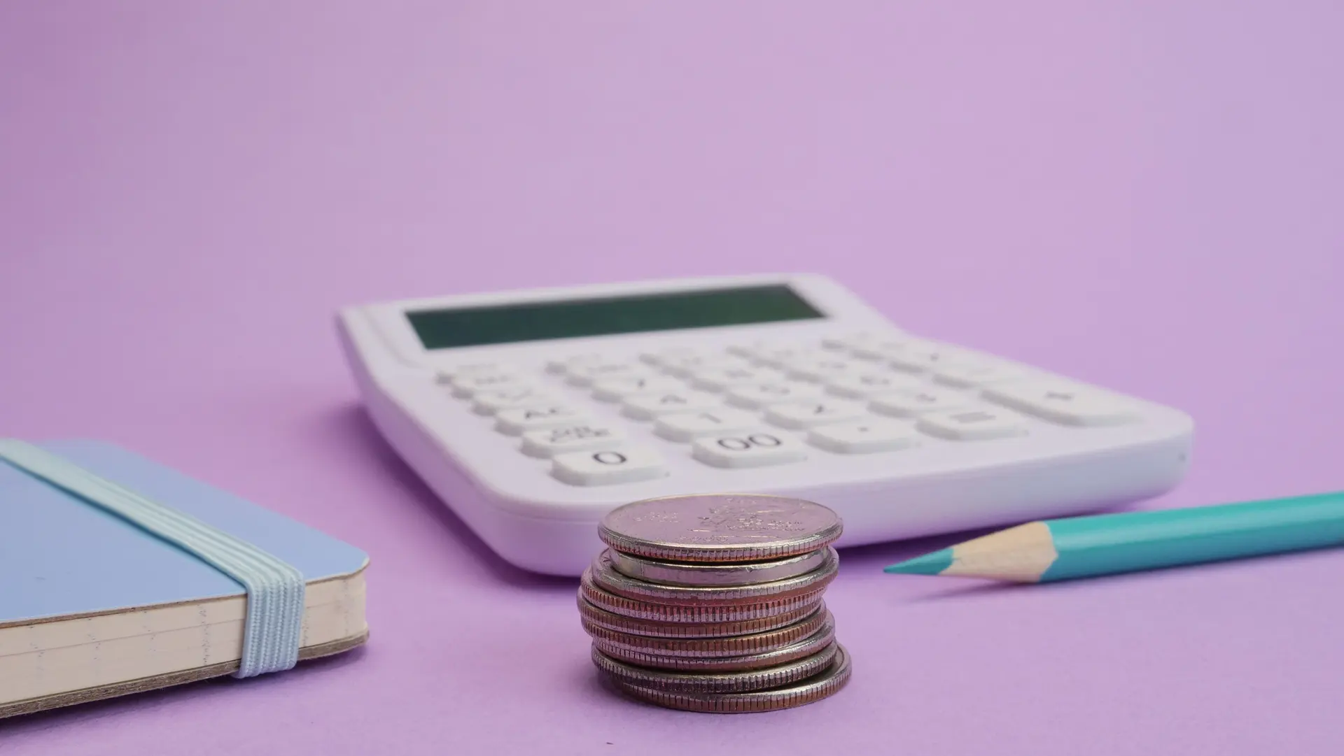 Calculadora, moedas e caderno de planejamento financeiro sobre fundo lilás