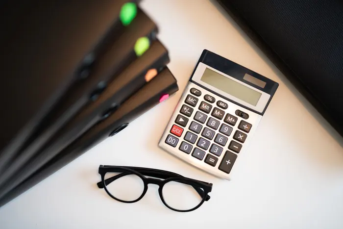 Calculadora, óculos e cadernos organizados sobre uma mesa clara