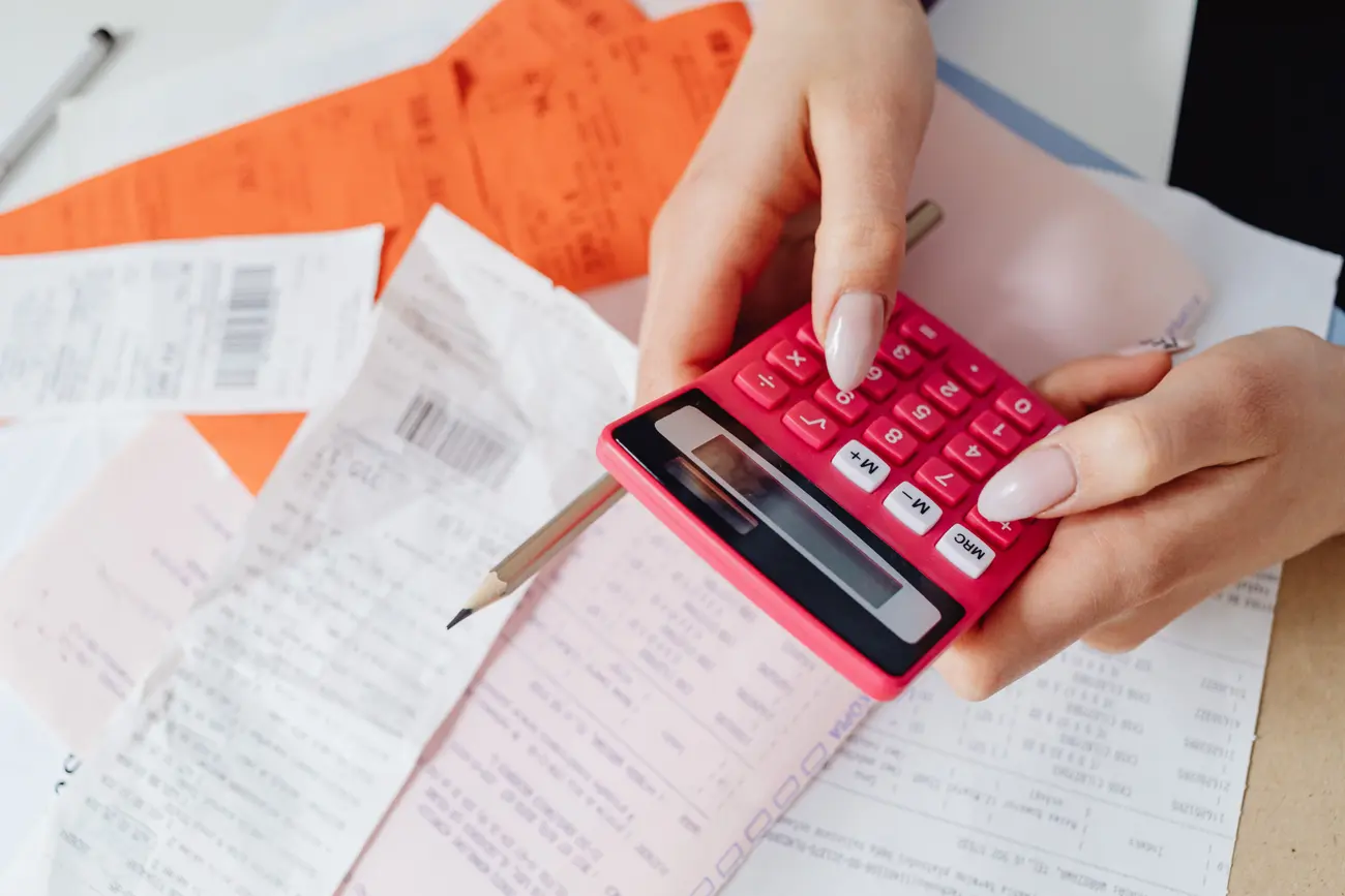 Calculadora vermelha sendo usada em cima de recibos e notas sobre a mesa