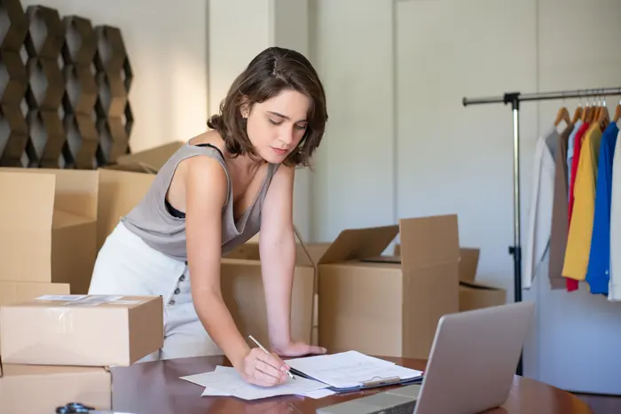 Empreendedora organizando pedidos com notebook e caixas de papelão ao lado
