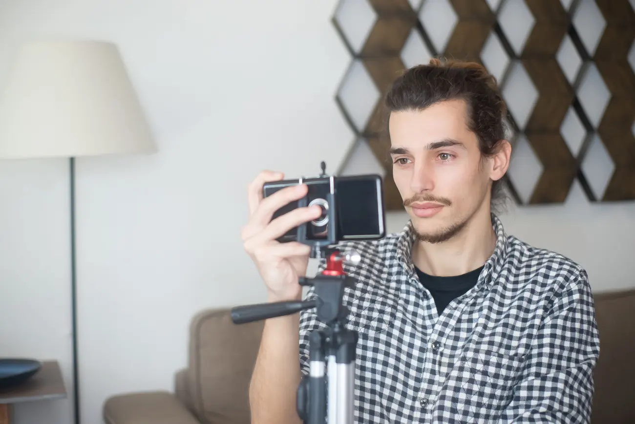 Homem gravando vídeo com o celular preso a um tripé numa sala iluminada