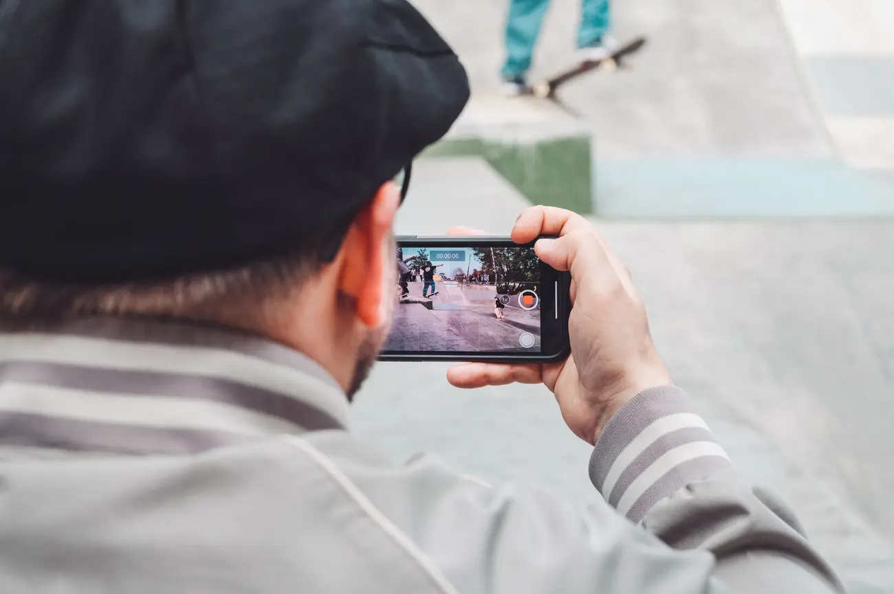 Homem filmando um skatista com o celular em um espaço urbano