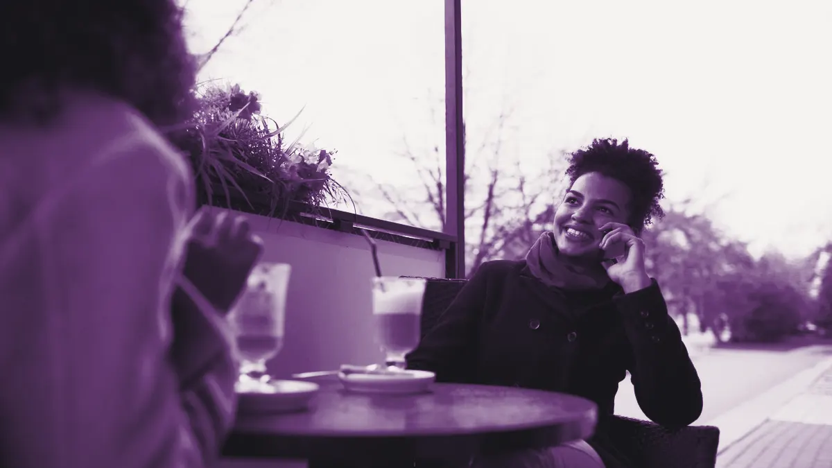 Mulher num café falando ao celular, sorrindo