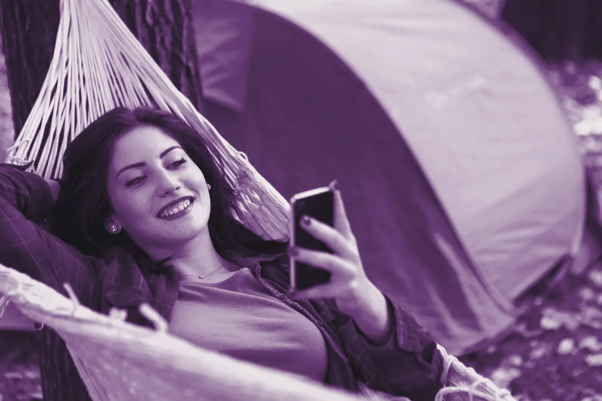 Mulher deitada numa rede, sorrindo para o celular